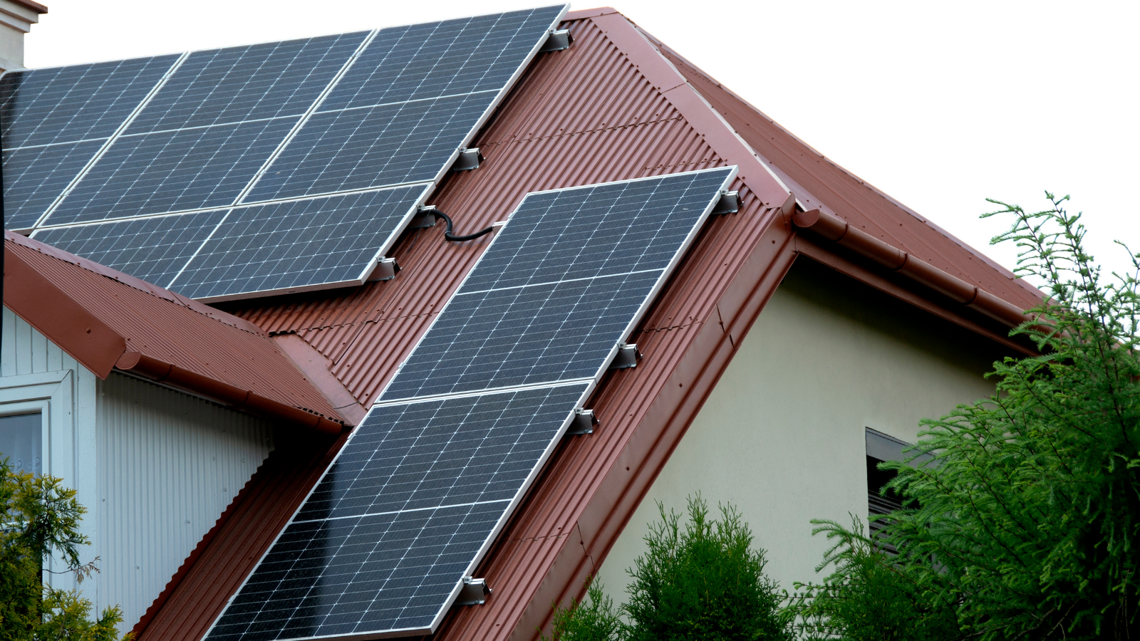 Zonnepanelen geïnstalleerd op een schuin rood dak, omgeven door groen, die zonlicht omzetten in elektriciteit