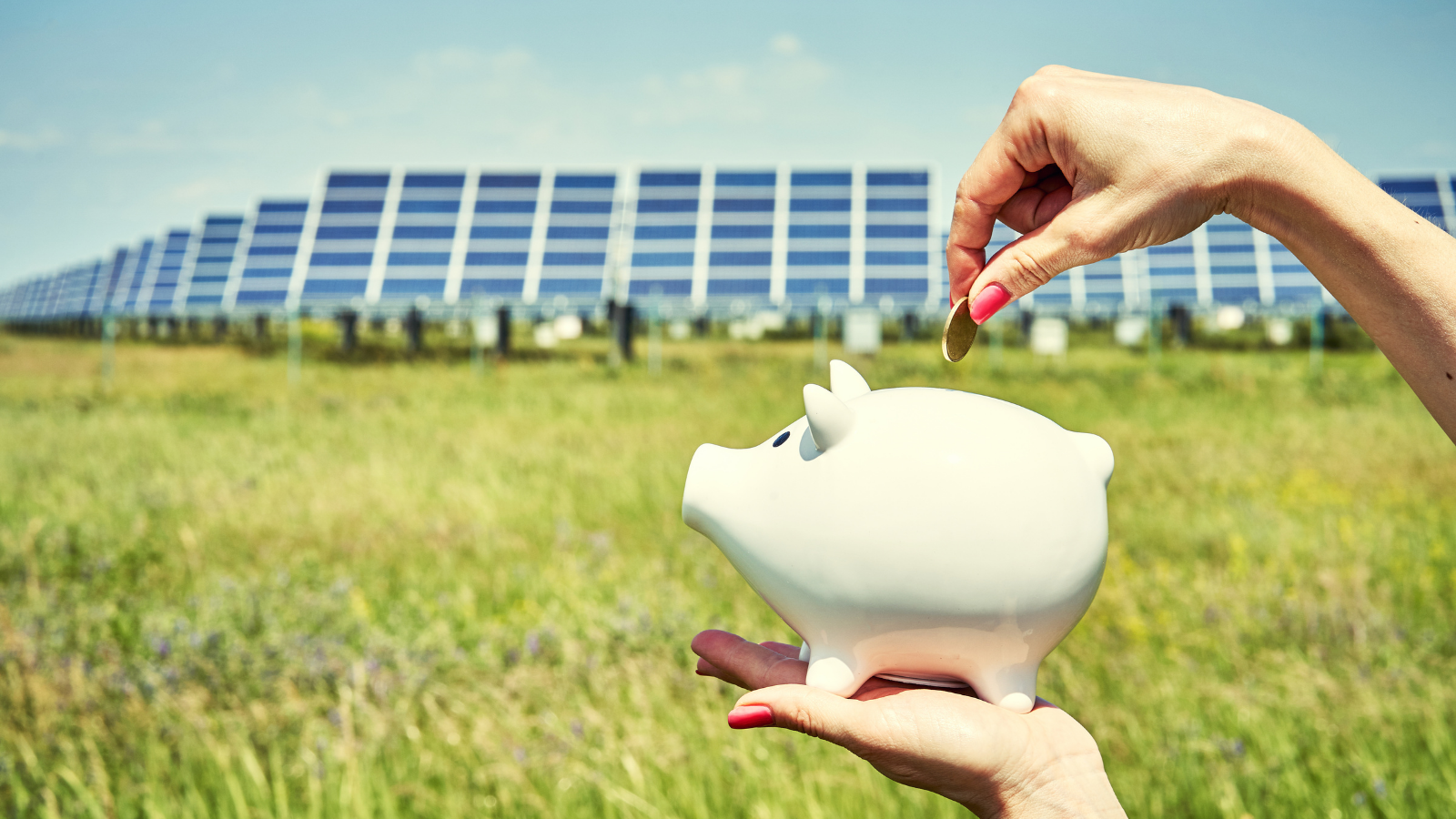 Hand die een munt in een spaarvarken stopt met zonnepanelen op de achtergrond.