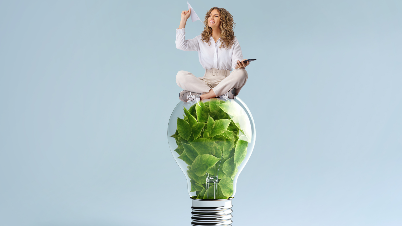 Vrouw zittend op een gloeilamp gevuld met groene bladeren, symboliseert duurzame energie.